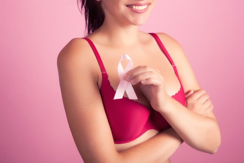 Woman in pink bra holding breast cancer awareness ribbon after breast reconstruction