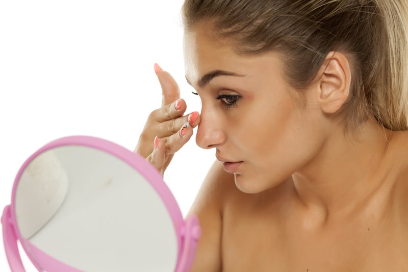 Woman looking in mirror touching nose, considering a rhinoplasty nose job