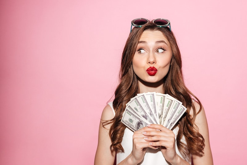 Stylish woman holding 100 dollar bills, thinking about financing plastic surgery